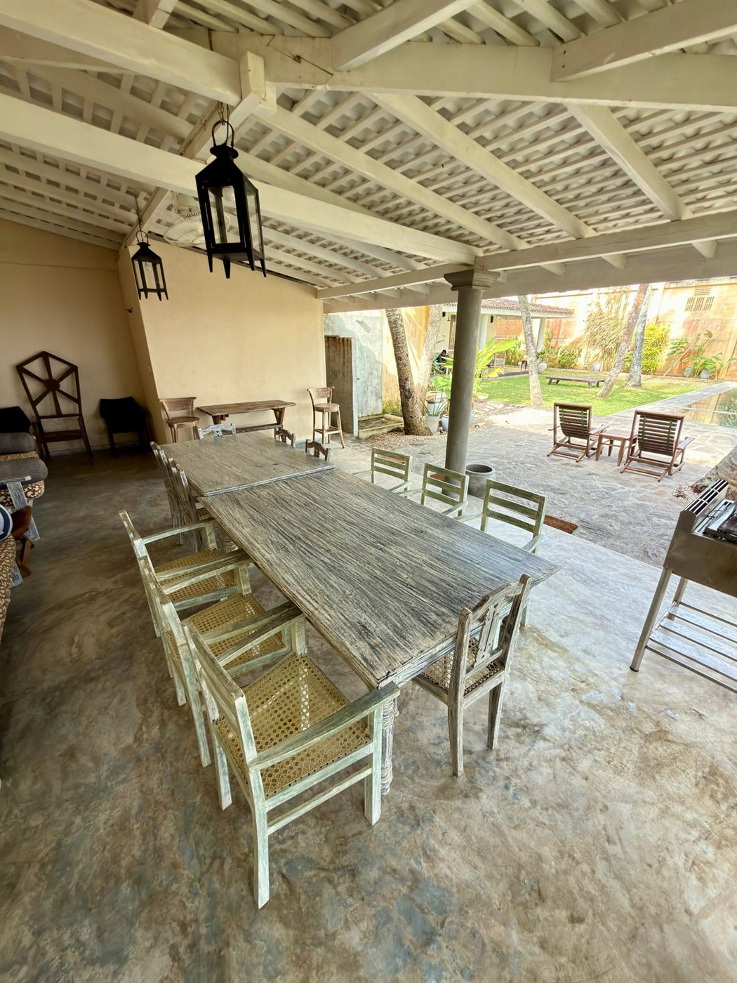 The open-air dining pavilion — long weathered-timber tables, cane chairs and hanging lanterns under a white pitched roof