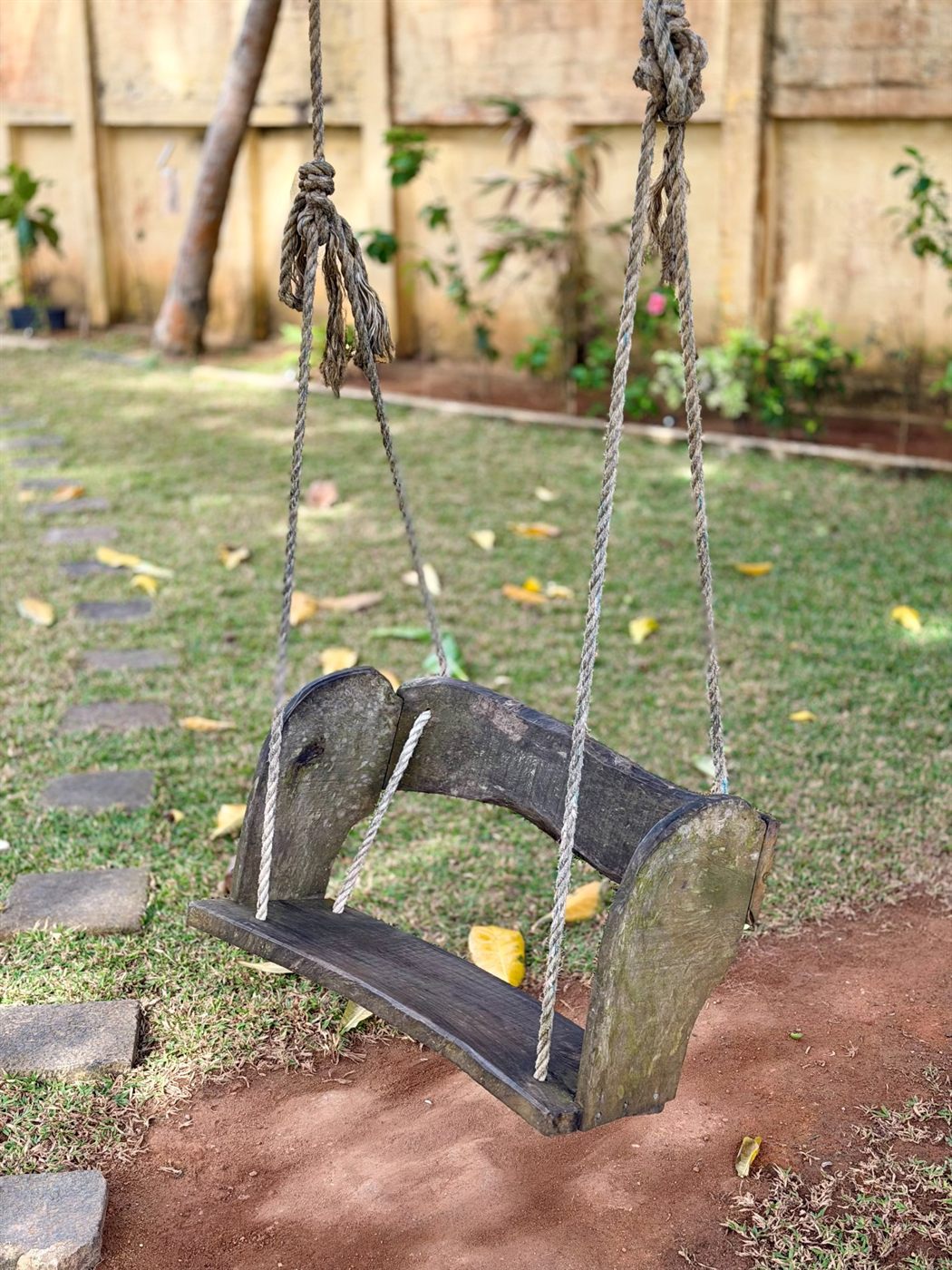 A rustic rope-and-timber swing hanging from a tree in the garden