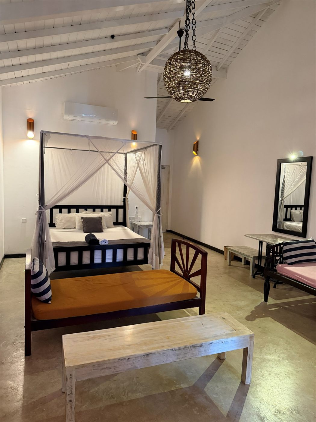 A four-poster bed with mosquito nets and an orange teak daybed in a family deluxe room with sea and river views