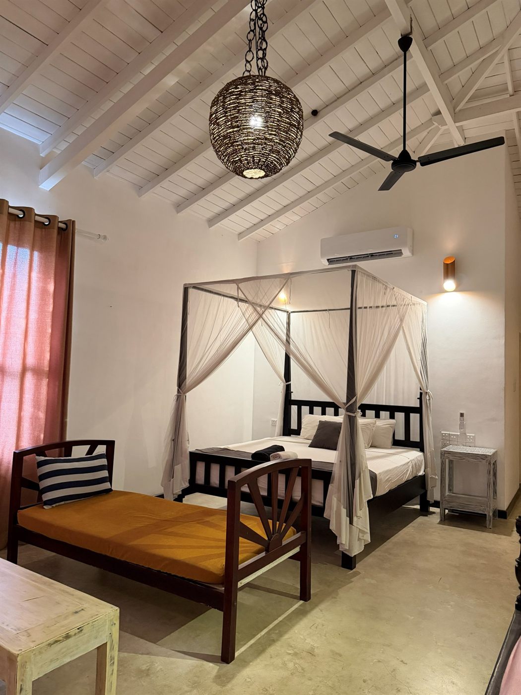 A four-poster bed with mosquito nets, a teak daybed and a ceiling fan in a ground-floor family deluxe room with sea views